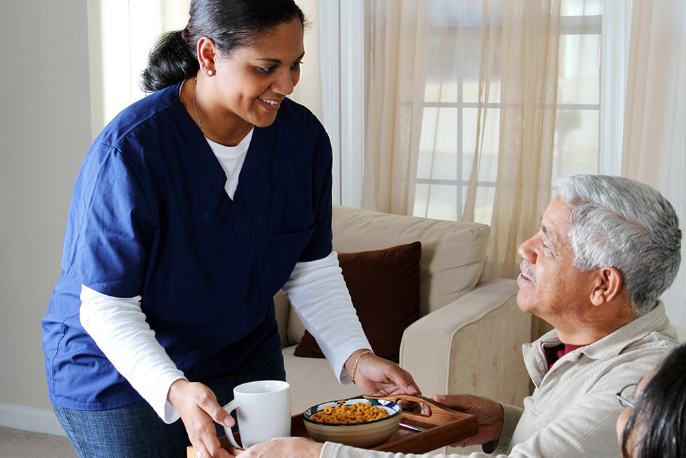 Care worker serving food on tray to senior man