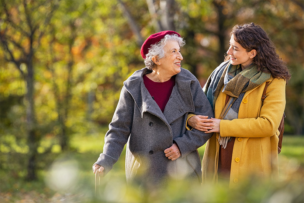 Smiling elderly woman and care worker walking outside together